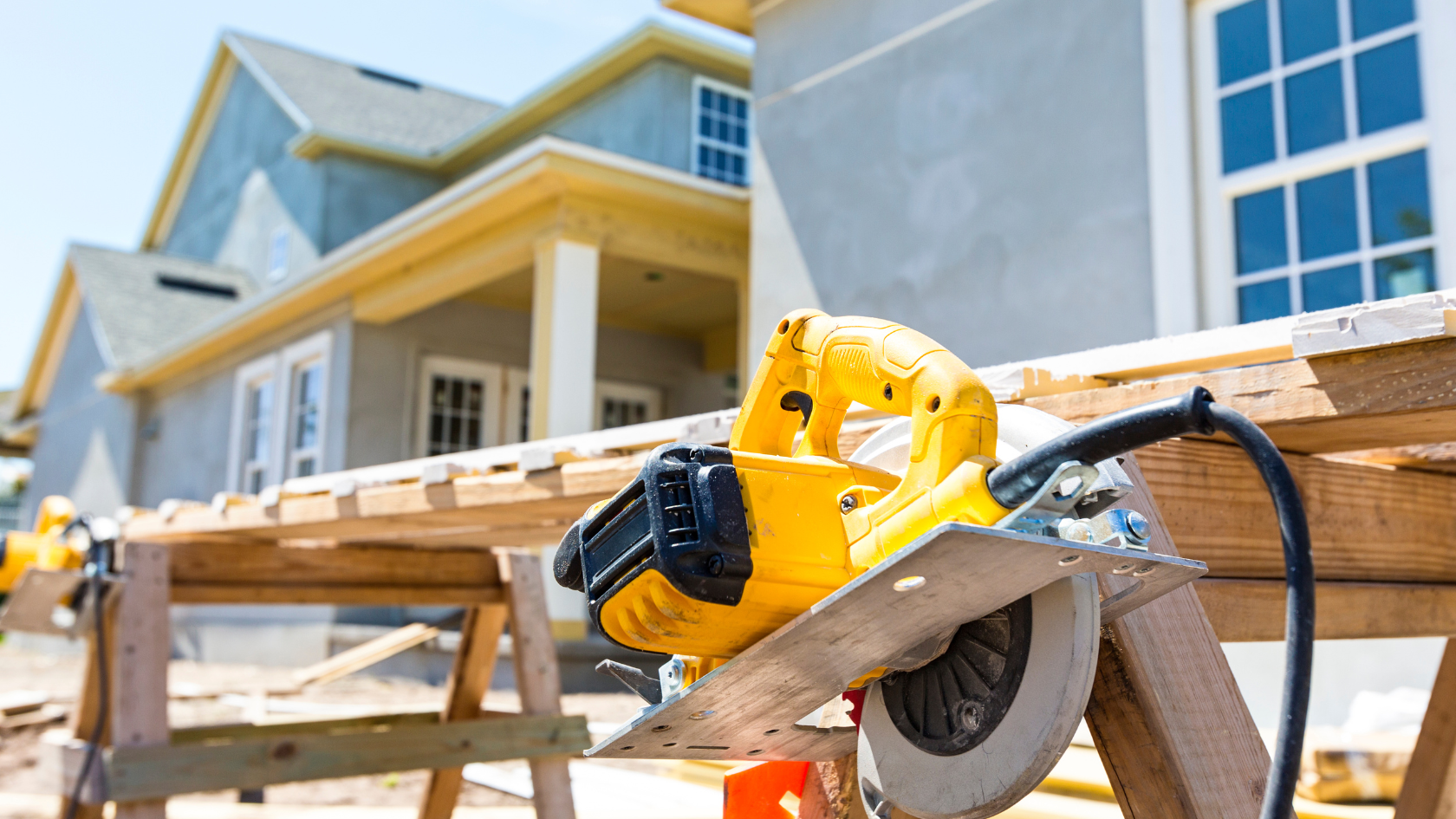 A cordless circular saw sits on a piece of wood in front of a house